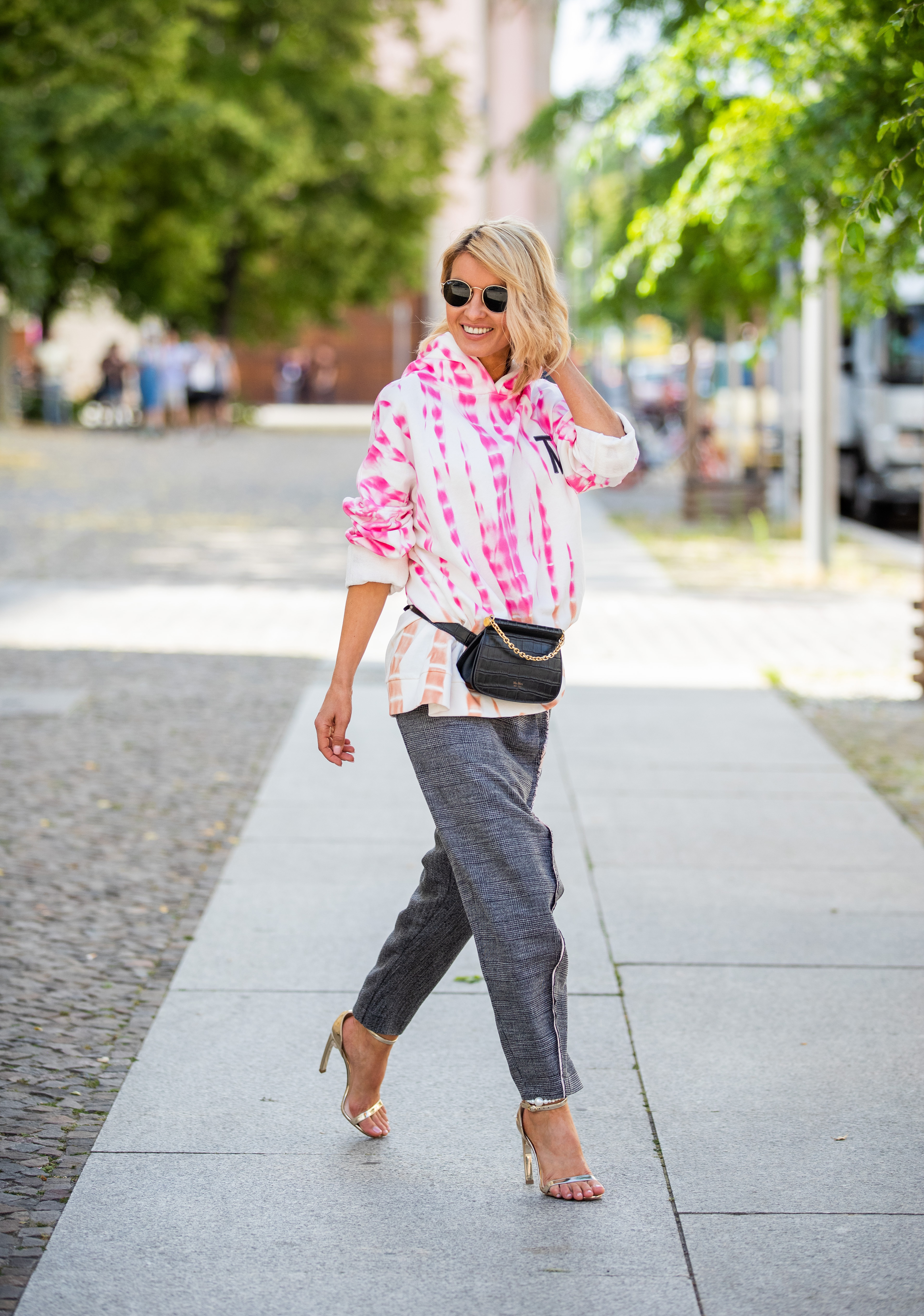 BERLIN, GERMANY - JULY 22: Gitta Banko is seen wearing a Tie dye oversized hoodie by Gitta Banko x The Mercer, an asymmetric pants by Balossa, a black belt bag by Max Mara, golden ankle-strap sandals with signature pearl embellishment at the junction of the heel and sole by Nicholas Kirkwood and sunglasses by Ray Ban on July 22, 2019 in Berlin, Germany. (Photo by Christian Vierig/Getty Images)